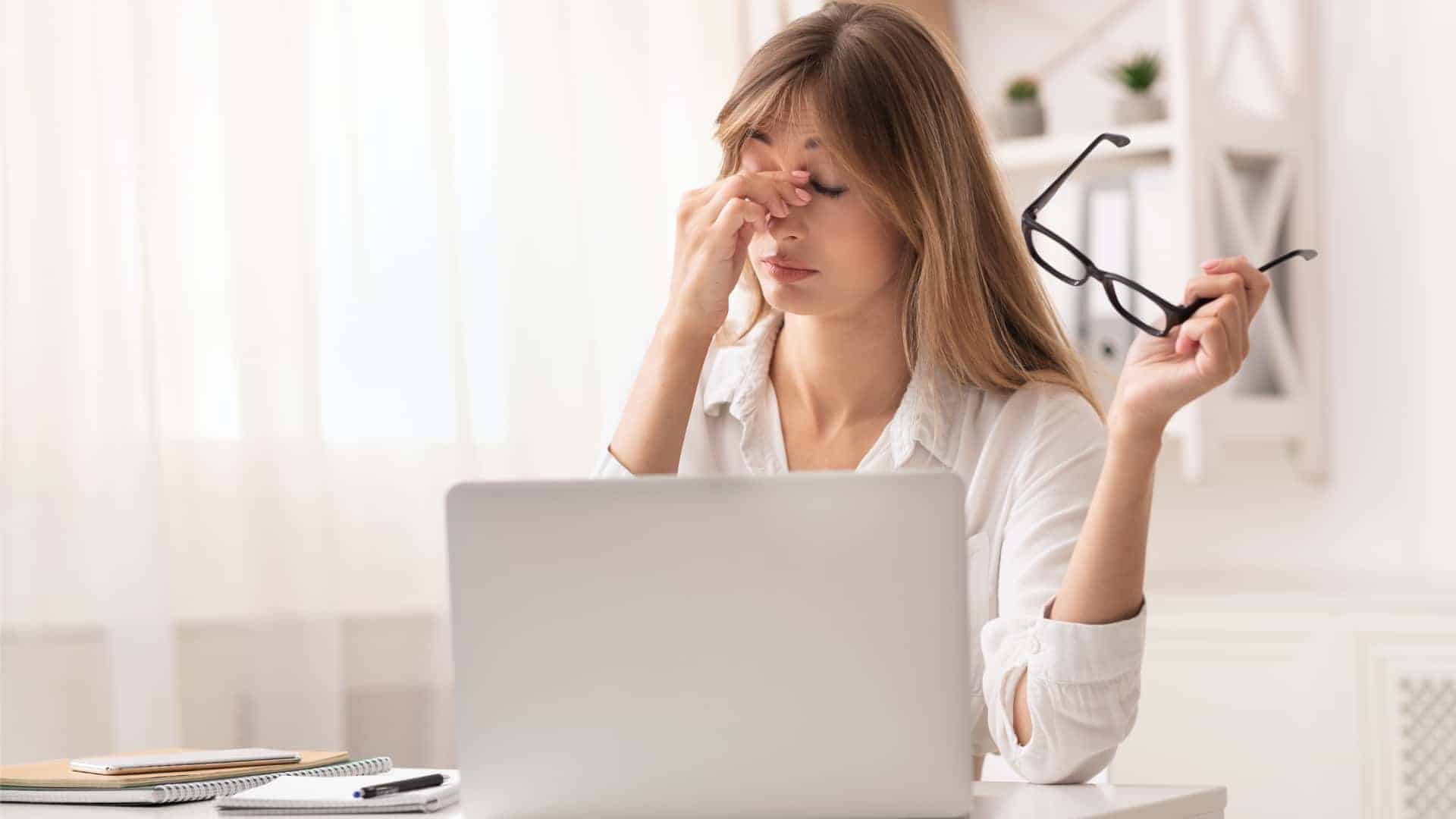 A woman holding her nose bridge while working on her laptop